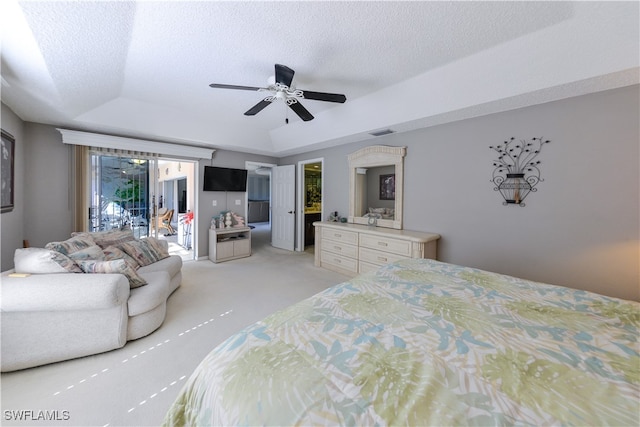 bedroom featuring ceiling fan, access to exterior, a textured ceiling, a tray ceiling, and light colored carpet