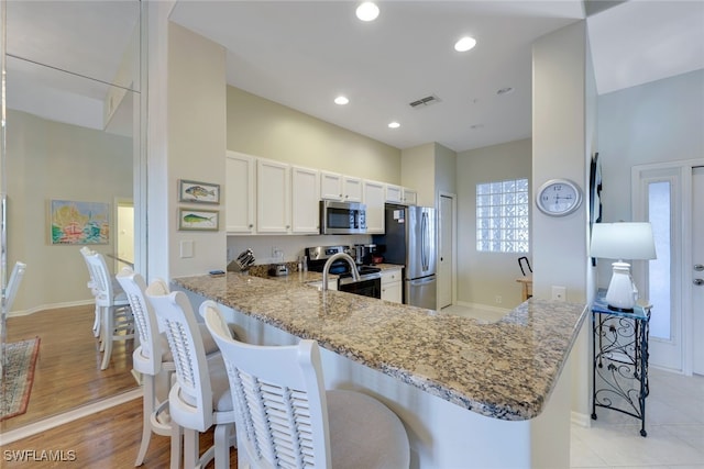 kitchen with kitchen peninsula, a breakfast bar, stainless steel appliances, and white cabinetry