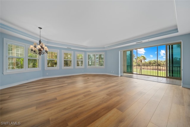 unfurnished room featuring a notable chandelier, light wood-type flooring, ornamental molding, and a tray ceiling