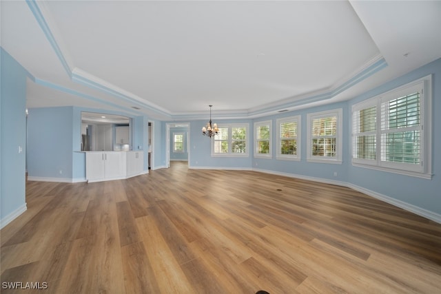 unfurnished living room with a raised ceiling, ornamental molding, light hardwood / wood-style floors, and a notable chandelier