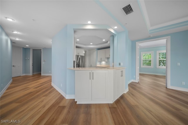 kitchen with white cabinets, wood-type flooring, ornamental molding, kitchen peninsula, and stainless steel refrigerator