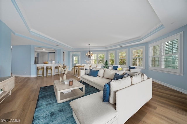 living room featuring hardwood / wood-style floors, a notable chandelier, ornamental molding, and a tray ceiling