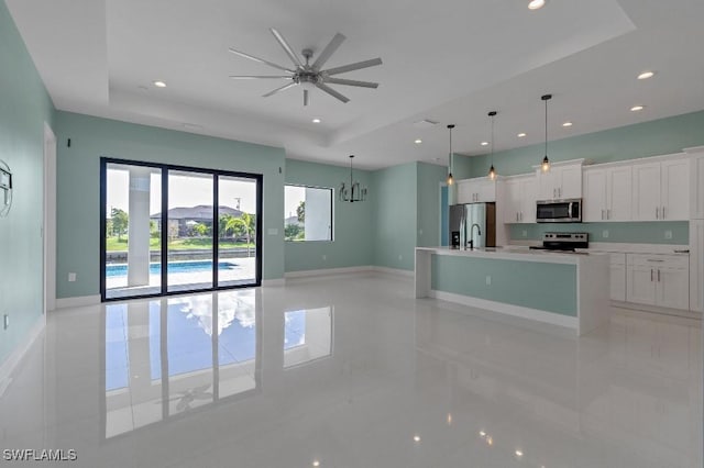 kitchen featuring ceiling fan with notable chandelier, appliances with stainless steel finishes, a tray ceiling, decorative light fixtures, and white cabinetry