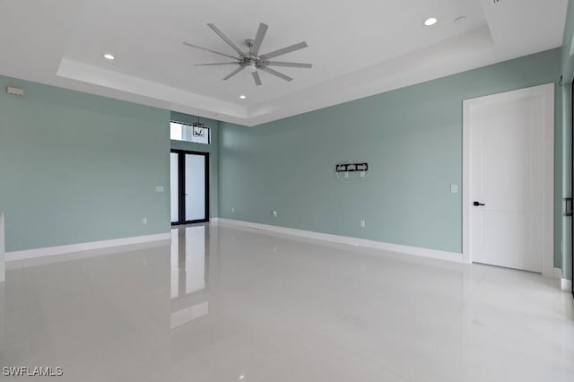 tiled spare room featuring a raised ceiling and ceiling fan