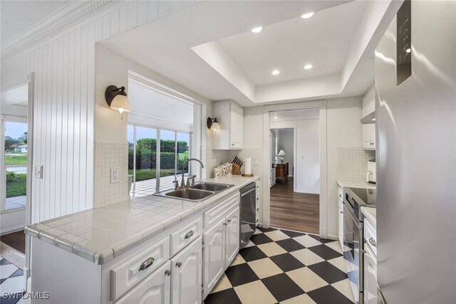 kitchen with sink, tile counters, decorative backsplash, white cabinets, and appliances with stainless steel finishes