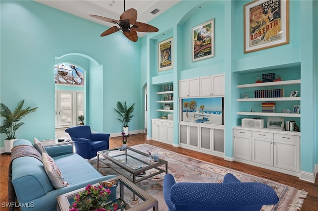 living room featuring built in shelves, ceiling fan, a high ceiling, and dark hardwood / wood-style floors