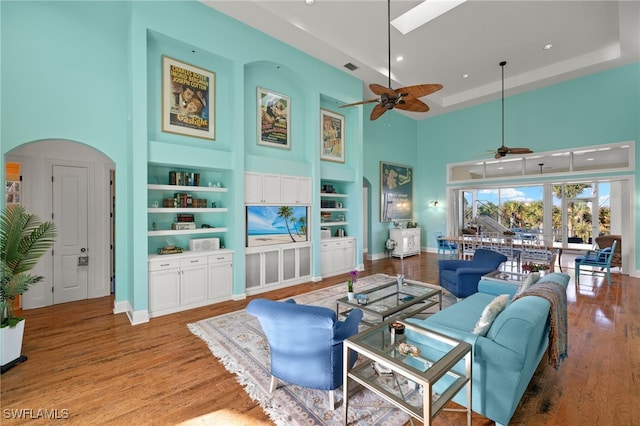 living room with ceiling fan, a towering ceiling, wood-type flooring, and built in features