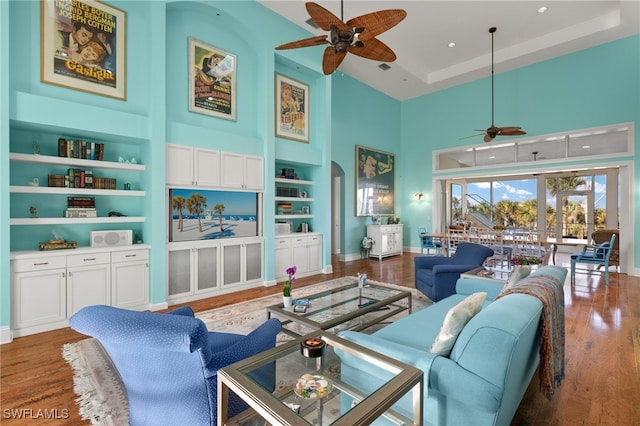 living room featuring built in features, a high ceiling, dark wood-type flooring, a tray ceiling, and ceiling fan