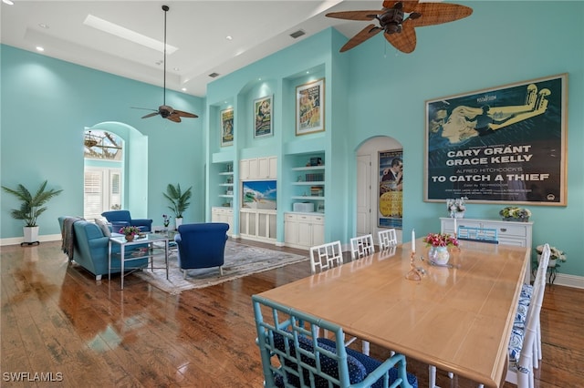 dining space featuring ceiling fan, a towering ceiling, dark hardwood / wood-style floors, and built in shelves