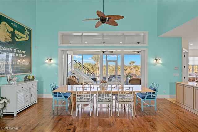 dining area with a wealth of natural light, wood-type flooring, ceiling fan, and a towering ceiling