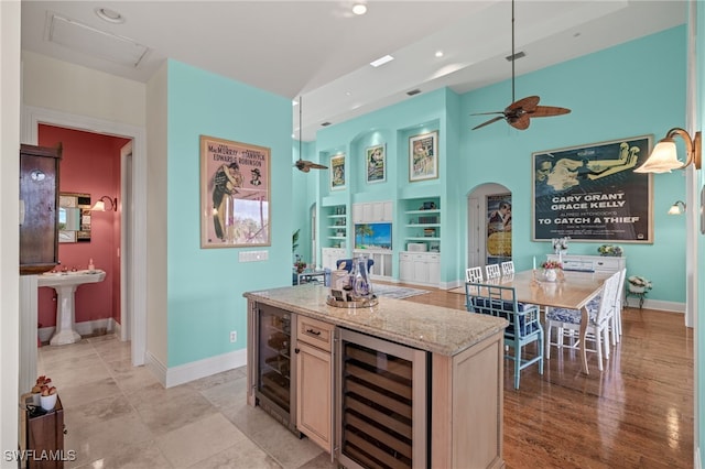 kitchen featuring light stone countertops, wine cooler, light wood-type flooring, and a center island