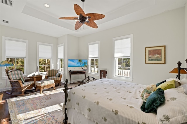 bedroom with a tray ceiling, wood-type flooring, and ceiling fan