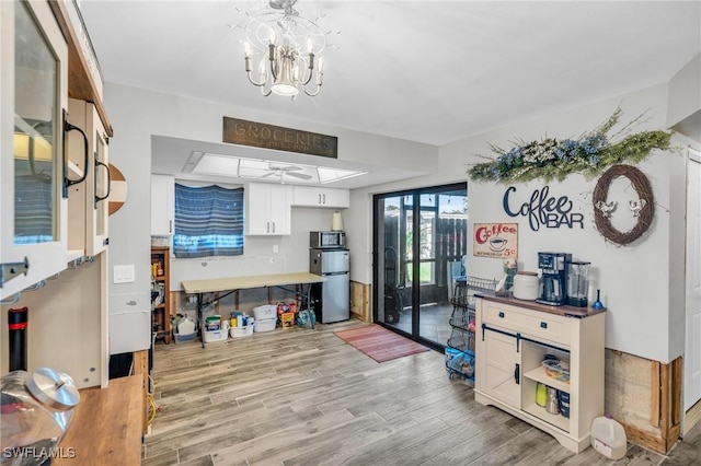 kitchen featuring white cabinets, appliances with stainless steel finishes, light wood-type flooring, and ceiling fan with notable chandelier