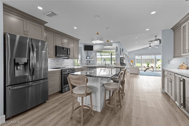 kitchen with light wood-type flooring, stainless steel appliances, vaulted ceiling, ceiling fan, and decorative light fixtures