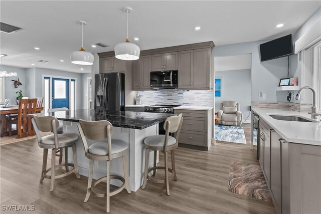 kitchen featuring sink, light wood-type flooring, stainless steel appliances, and hanging light fixtures