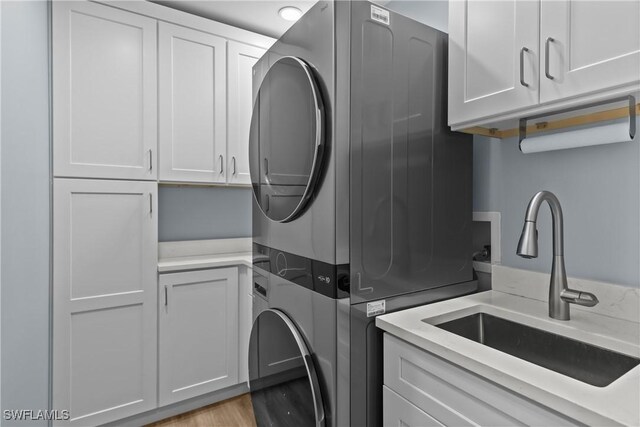 washroom featuring sink, cabinets, light wood-type flooring, and stacked washer / dryer