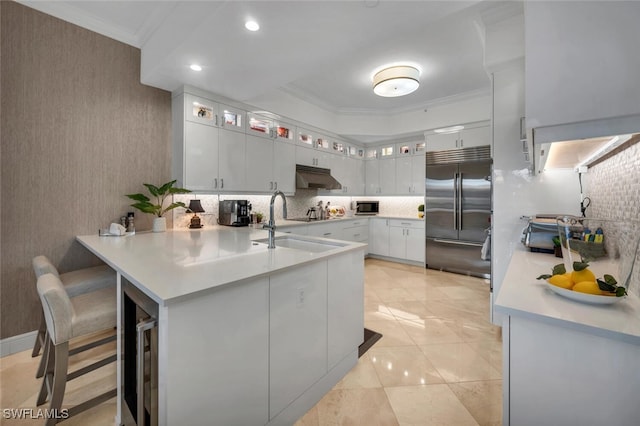 kitchen featuring stainless steel built in refrigerator, a breakfast bar, white cabinetry, ornamental molding, and kitchen peninsula