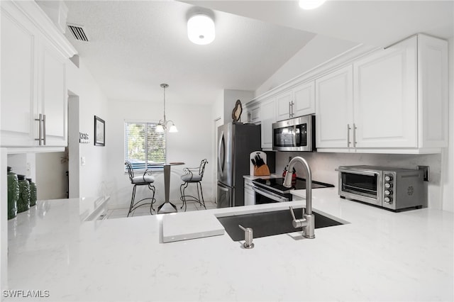 kitchen featuring lofted ceiling, white cabinets, sink, hanging light fixtures, and appliances with stainless steel finishes