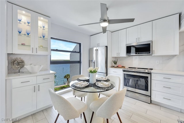 kitchen with white cabinetry, ceiling fan, stainless steel appliances, backsplash, and a water view