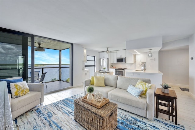 living room with ceiling fan, sink, a wall of windows, light hardwood / wood-style floors, and a water view