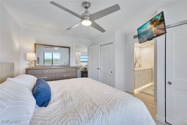 bedroom with light wood-type flooring, ceiling fan, and connected bathroom