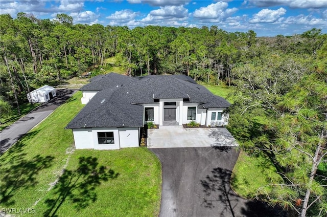 219 33rd Ave NW, Naples, FL 34120 - view of front of property with asphalt driveway, a wooded view, stucco siding, a front yard, and roof with shingles