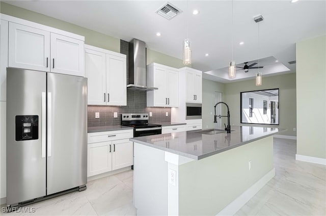 kitchen featuring sink, stainless steel appliances, wall chimney range hood, an island with sink, and decorative light fixtures