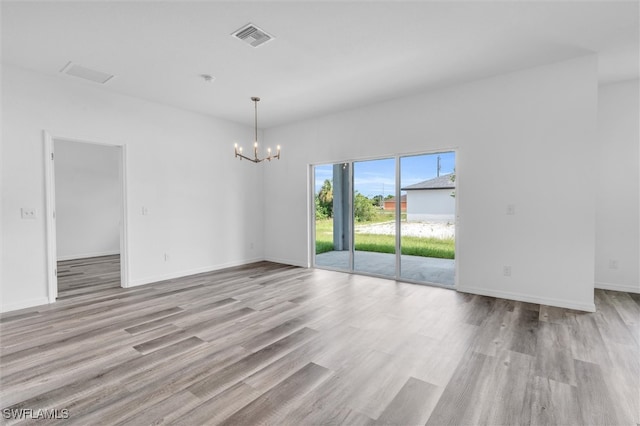 empty room featuring a notable chandelier and light wood-type flooring