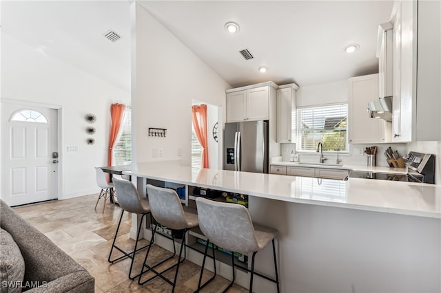 kitchen featuring kitchen peninsula, stainless steel appliances, vaulted ceiling, and a breakfast bar