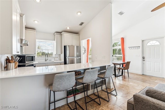 kitchen featuring kitchen peninsula, appliances with stainless steel finishes, a kitchen breakfast bar, white cabinets, and vaulted ceiling