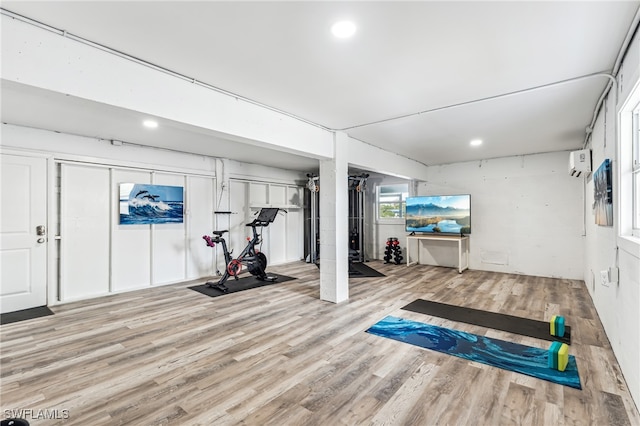 exercise room with a wall unit AC and light hardwood / wood-style floors