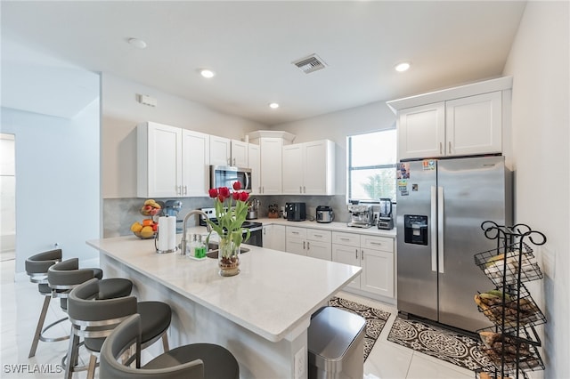 kitchen with stainless steel appliances, white cabinets, decorative backsplash, kitchen peninsula, and a breakfast bar area