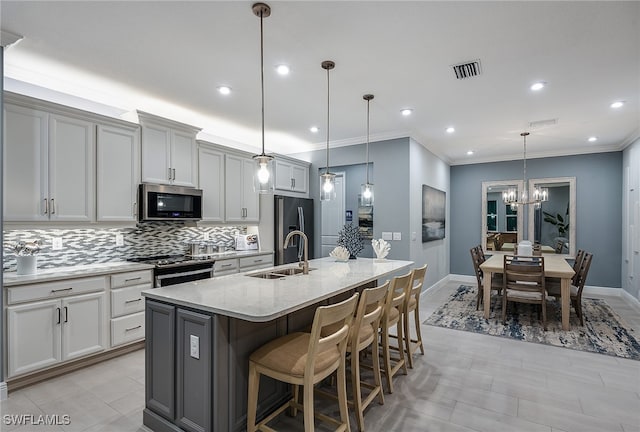 kitchen with appliances with stainless steel finishes, sink, a center island with sink, and hanging light fixtures