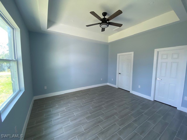 unfurnished bedroom with dark wood-type flooring, ceiling fan, and a tray ceiling