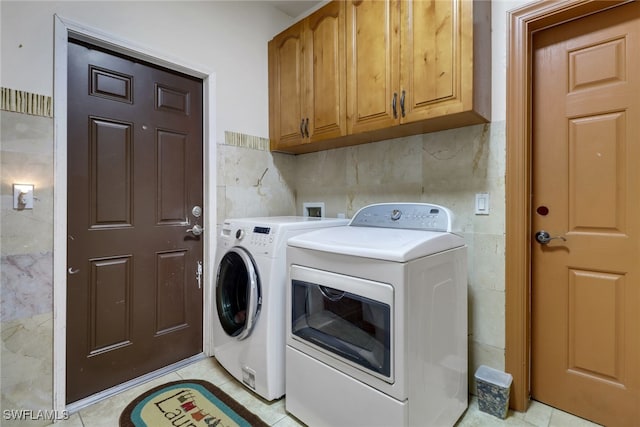 clothes washing area with tile walls, separate washer and dryer, cabinets, and light tile patterned floors