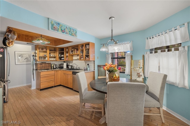 kitchen featuring sink, light hardwood / wood-style flooring, appliances with stainless steel finishes, tasteful backsplash, and decorative light fixtures