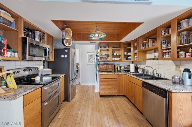 kitchen with backsplash, light stone counters, stainless steel appliances, sink, and light hardwood / wood-style flooring