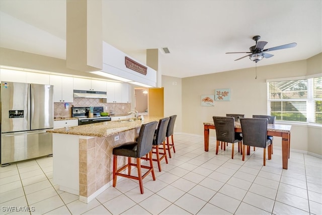 kitchen with light stone countertops, stainless steel appliances, sink, white cabinetry, and a breakfast bar area