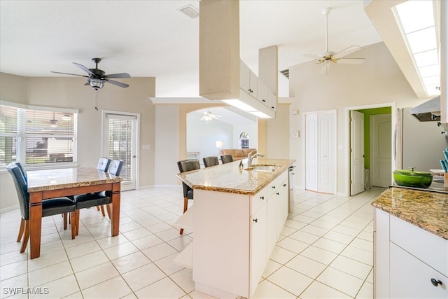 kitchen with white cabinets, a center island with sink, light stone countertops, and sink