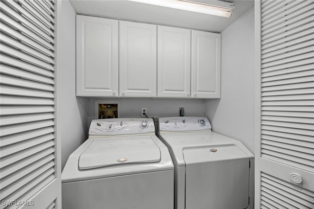 clothes washing area with washing machine and dryer, cabinets, and a textured ceiling