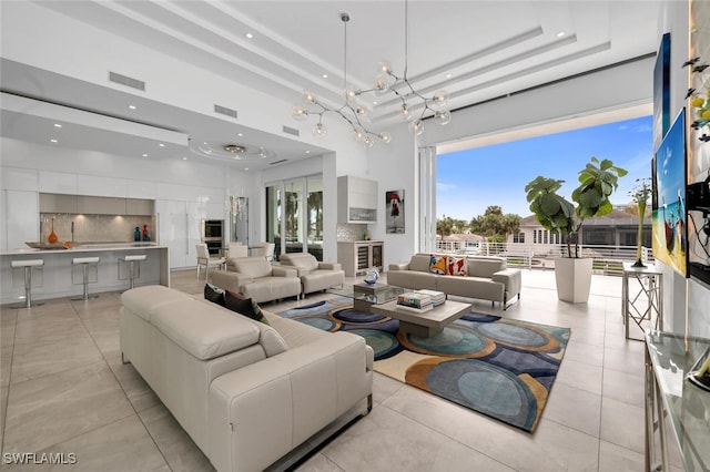 tiled living room featuring a notable chandelier, a tray ceiling, and a high ceiling