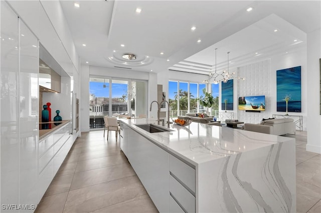 kitchen with light stone counters, white cabinets, sink, and a large island with sink