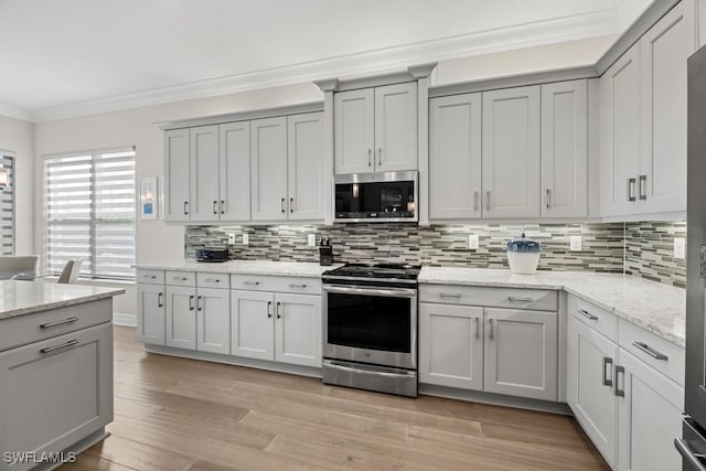 kitchen with light hardwood / wood-style floors, light stone counters, decorative backsplash, crown molding, and appliances with stainless steel finishes