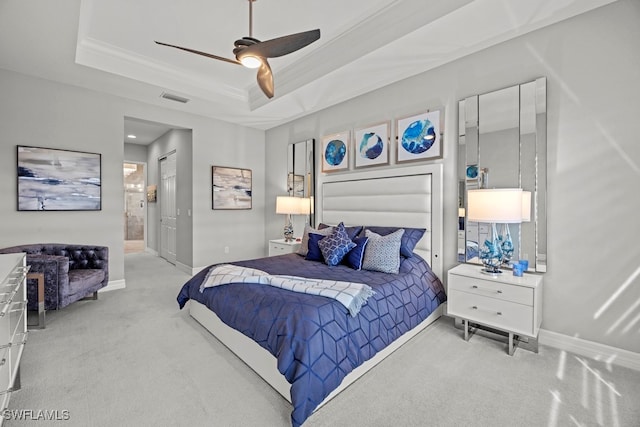 bedroom with a tray ceiling, light carpet, ceiling fan, and ensuite bath