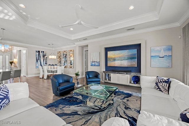 living room featuring ornamental molding, ceiling fan with notable chandelier, wood-type flooring, and a tray ceiling