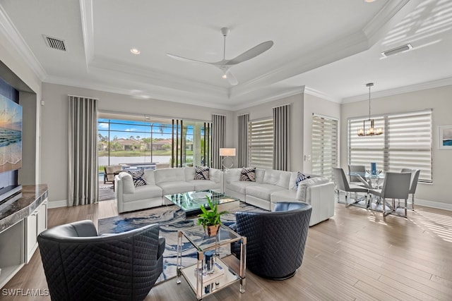 living room featuring light hardwood / wood-style floors, ceiling fan with notable chandelier, a raised ceiling, and crown molding