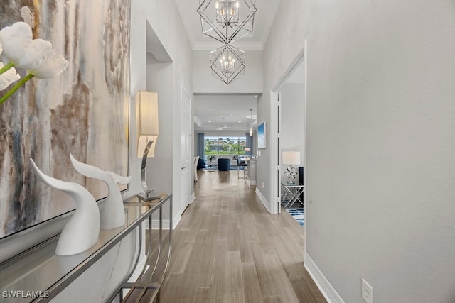 corridor with ornamental molding, hardwood / wood-style flooring, a high ceiling, and an inviting chandelier