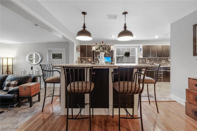 kitchen featuring dark brown cabinetry, hanging light fixtures, a breakfast bar area, backsplash, and light wood-type flooring