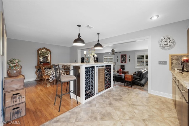 kitchen featuring light hardwood / wood-style floors, a breakfast bar area, ceiling fan, light stone countertops, and decorative light fixtures