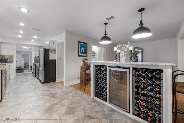 interior space with white cabinets, backsplash, stainless steel refrigerator, decorative light fixtures, and wine cooler